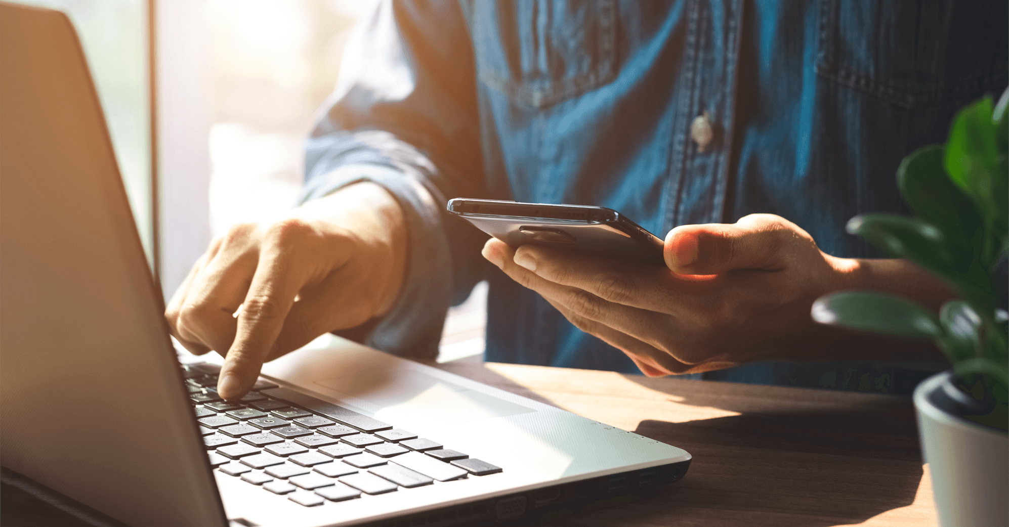 Main pointant sur un clavier d'ordinateur et smartphone dans l'autre main